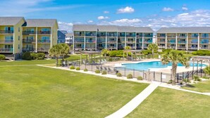 A hotel with multiple floors, a swimming pool, and a well-maintained lawn. - Ocean Vue - 1BR Surf Condo - Swimming Pool & Ocean Views! (Surf City)