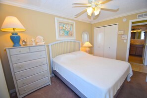 A bedroom with a bed, dresser, ceiling fan, and a door leading to a bathroom.