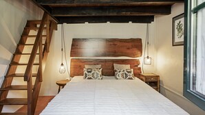 A bedroom with a wooden headboard, a ladder, a bed with patterned pillows, a bedside table, and a framed picture on the wall. - In Laurissilva Forest, Casa do Lanço -Carvalho (São Vicente)