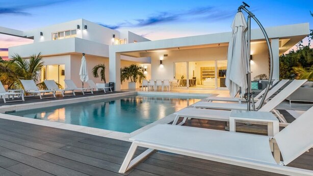 A modern pool area with lounge chairs and a pool, surrounded by a two-story building with large windows and outdoor lighting.