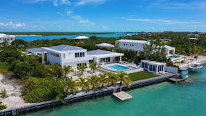 A coastal property with a swimming pool, multiple buildings, and a dock extending into turquoise waters.