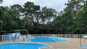 Une piscine avec un toboggan, entourée d’une clôture blanche et d’arbres.