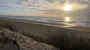 Une plage avec un sentier de sable menant à l’eau, une clôture en bois et une personne debout près de l’eau.
