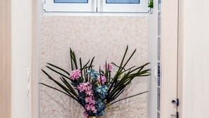Un pasillo con piso de mármol, un jarrón decorativo con flores y una ventana arriba.