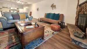 Uma sala de estar com um sofá azul, um sofá marrom, uma mesa de centro de madeira e um tapete estampado.