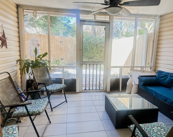 Relax in this serene sunroom with a sofa, armchair, and coffee table, surrounded by lush greenery and a view of the garden.