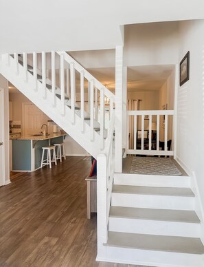 Stairs lead to an upper level, flanked by a kitchen area with a bar counter and stools.