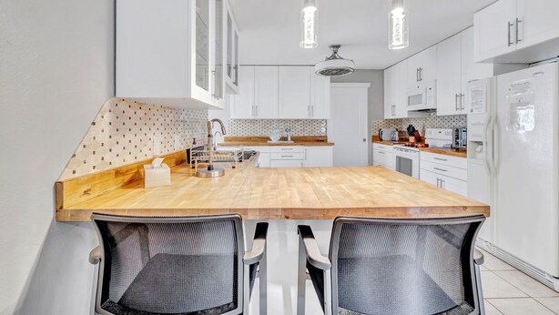 Una cucina moderna con isola in legno, pensili bianchi e illuminazione a sospensione.