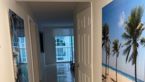 Een gang met een betegelde vloer, een deur naar een balkon en een wanddecoratie met een strandthema.