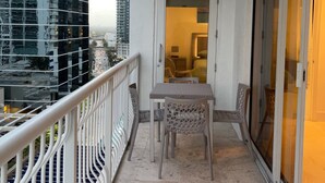 Een balkon met een tafel en stoelen, een schuifpui en uitzicht op hoge gebouwen.