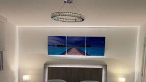 Een moderne slaapkamer met een groot bed, een hoofdbord, twee nachtkastjes met lampen, een plafondlamp en een schilderij van een pier aan de muur.