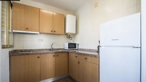 A compact kitchen with wooden cabinets, a white refrigerator, and a microwave on the countertop. - AQUARIUM II 8-3 (Benidorm)