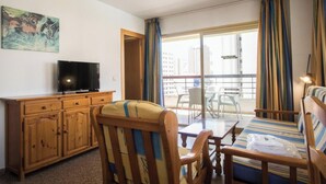 A hotel room with a wooden cabinet, a television, a striped sofa, a dining table, and a balcony with curtains. - AQUARIUM II 9-3 (Benidorm)