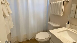 Ein kleines Badezimmer mit Toilette, Waschbecken, Duschvorhang und Handtuchhalter.