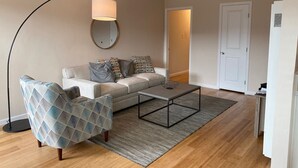 Ein modernes Wohnzimmer mit einer Couch, einem gemusterten Sessel, einem Couchtisch, einer Stehlampe und einem Spiegel an der Wand.