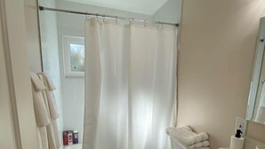 Une salle de bain avec un rideau de douche, des toilettes, un lavabo et une petite fenêtre.