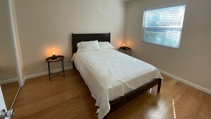 Une chambre à coucher avec un lit, deux tables de chevet, une fenêtre avec des stores et une porte.