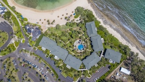 Vista aérea de un resort con piscina central, varias edificaciones, playa y zonas de estacionamiento.