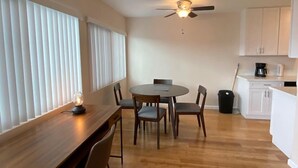 Une cuisine moderne avec des meubles blancs, un coin repas doté d’une table et de chaises en bois, et un ventilateur de plafond.