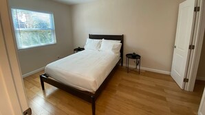 Une chambre à coucher avec un lit, une table de chevet, une fenêtre avec des stores et une porte.