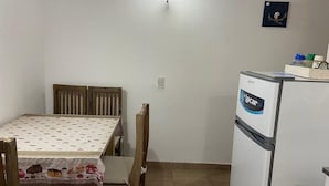 Une petite cuisine équipée d’un réfrigérateur, d’une table à manger avec des chaises et d’un luminaire fixé au mur.