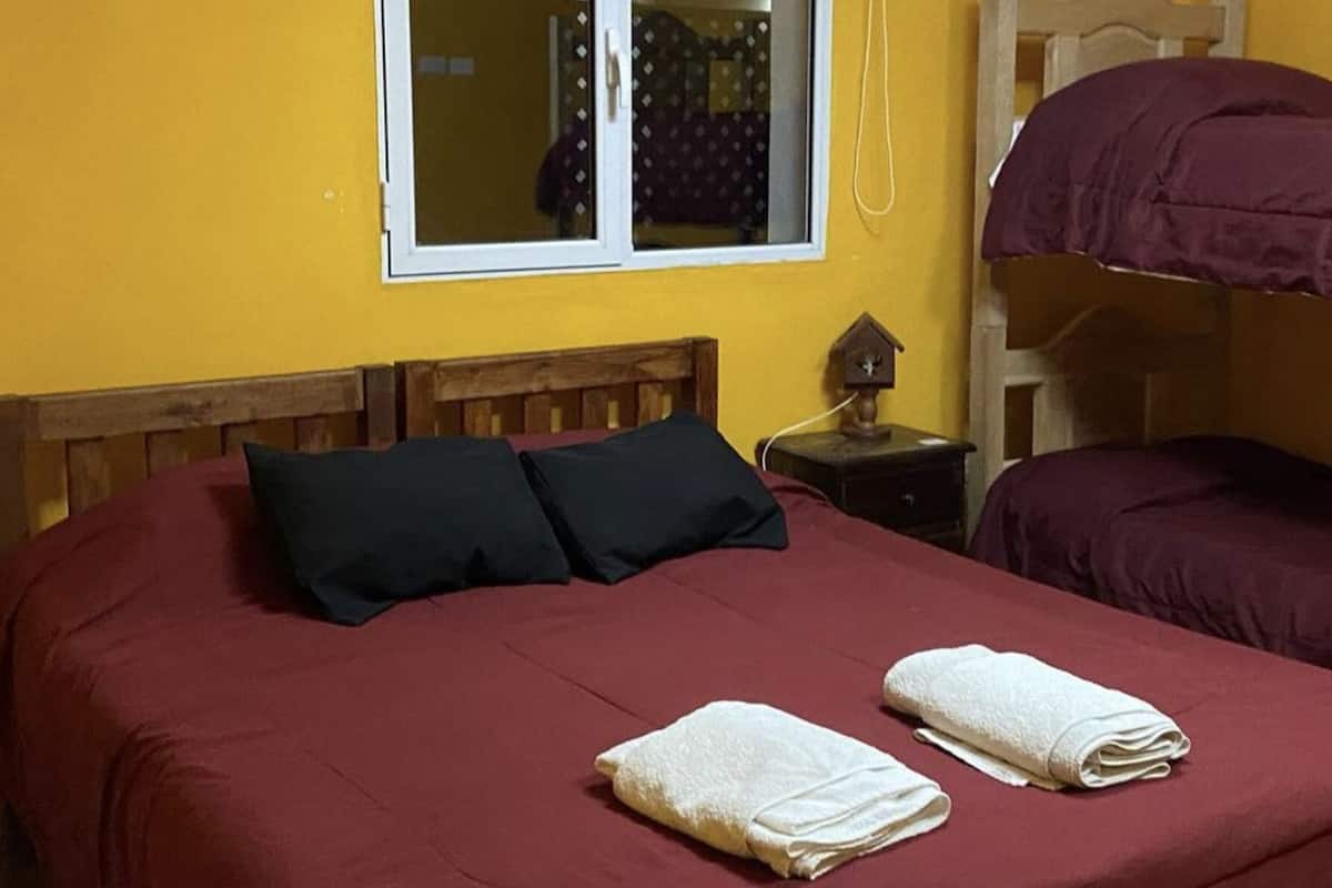 Habitación individual con una cama de una sola plaza, cabecero de madera, ventana con persiana blanca y mesita de noche con lámpara.