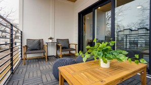 Un balcón con suelo de madera, dos sillones de mimbre con cojines, una mesita y una planta en maceta.