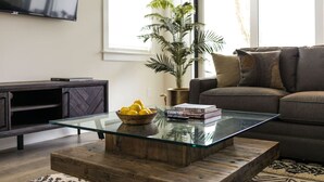 Una sala de estar moderna con una mesa de centro de vidrio, un sofá, un televisor y una planta en maceta.