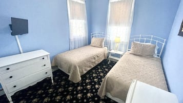 Una habitación con dos camas individuales, un tocador blanco, una mesita con lámpara y un televisor montado en la pared.