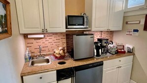 A compact kitchen with white cabinets, a microwave, a coffee maker, and a dishwasher. - Quaker Inn (Ocean Grove)