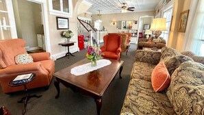 A spacious living room with a high ceiling, a staircase, and a view into the dining area. - Quaker Inn (Ocean Grove)
