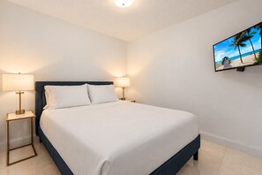 Une chambre d’hôtel avec un lit, deux lampes de chevet, un téléviseur fixé au mur et un sol carrelé.