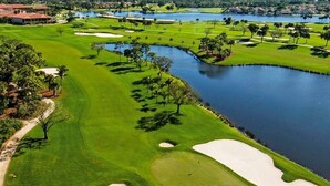 Un campo de golf con búnkeres de arena, obstáculos de agua y una vista del horizonte de la ciudad al fondo.
