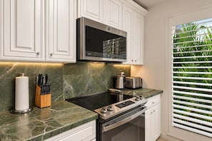 A kitchen with white cabinets, a stainless steel microwave, a stove, and a toaster.