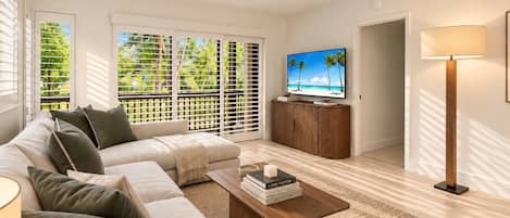 A modern living room with a sectional sofa, a coffee table with books, a flat-screen TV, and a floor lamp.
