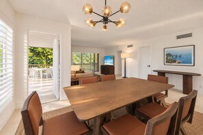 Un vaste espace dédié à la salle à manger, avec une grande table en bois et des chaises en cuir, un lustre moderne et une vue sur un patio extérieur luxuriant.