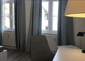 Relax in comfort with a chair by the window, a table for dining or reading, and a lamp for ambiance.