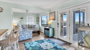 A cozy living room with a sofa, chairs, a dining table, and a large window with a view. - Summer Salt: Amazing Ocean, Marsh and Lighthouse Views (Caswell Beach)