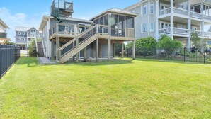 A multi-story residential building with a wooden deck, a staircase, and a fenced yard. - Summer Salt: Amazing Ocean, Marsh and Lighthouse Views (Caswell Beach)