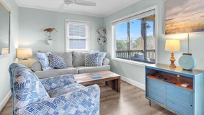 A living room with a sofa, two patterned armchairs, a coffee table, a blue cabinet, a ceiling fan, and a window with blinds. - Summer Salt: Amazing Ocean, Marsh and Lighthouse Views (Caswell Beach)
