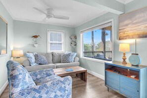 Ein Wohnzimmer mit einer Couch, zwei gemusterten Sesseln, einem Couchtisch, einem blauen Schrank, einem Deckenventilator und einem Fenster mit Jalousien.