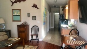 A living room with a wooden coffee table, a sofa, and a dining table with chairs. There are wall decorations including a shark and a framed picture.