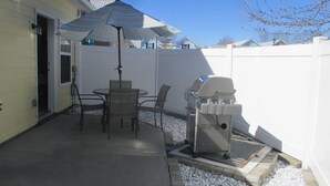 A patio with a table and chairs, a grill, and a covered umbrella.