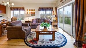 Ein geräumiges Wohnzimmer mit großem Fenster, einem Holztisch, Ledersofas und einem Essbereich mit Holztisch und Stühlen.