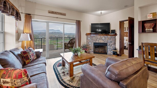 Ein Wohnzimmer mit Kamin aus Stein, Ledersofas, einem Fernseher und Blick ins Freie.