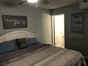 A bedroom with a bed, a wall with a sign saying "This is the good life," and another sign that says "The Beach is our Happy Place."