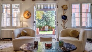 Una habitación acogedora con dos sillones cómodos, una mesa de centro de mármol y vistas a un jardín a través de una puerta abierta.