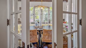 Una habitación con un techo de madera grande, una mesa de comedor con sillas, y vistas a otra habitación con una estantería y adornos a través de una puerta de cristal.