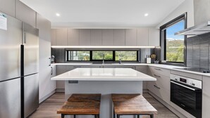 A modern kitchen with a central island, stainless steel appliances, and a large window providing a view of greenery.