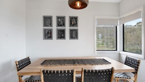 Un coin repas avec une table en bois, six chaises en osier et six dessins techniques encadrés accrochés au mur.